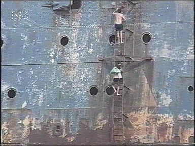 TWO LOCALS CLIMB UP THE SIDE OF THE HULL.